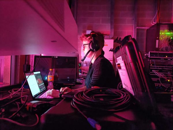 Side view of Anna in a projection box of a theatre wearing comms