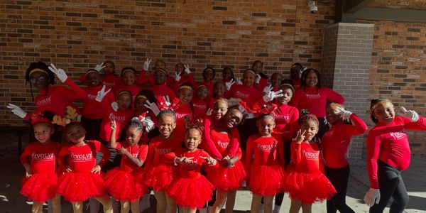 Young dancers in red outfits posing happily together outdoors.