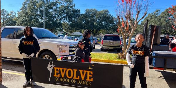 Children holding an Evolve School of Dance banner outdoors.