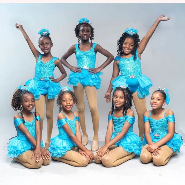 Seven young dancers in blue costumes posing together.