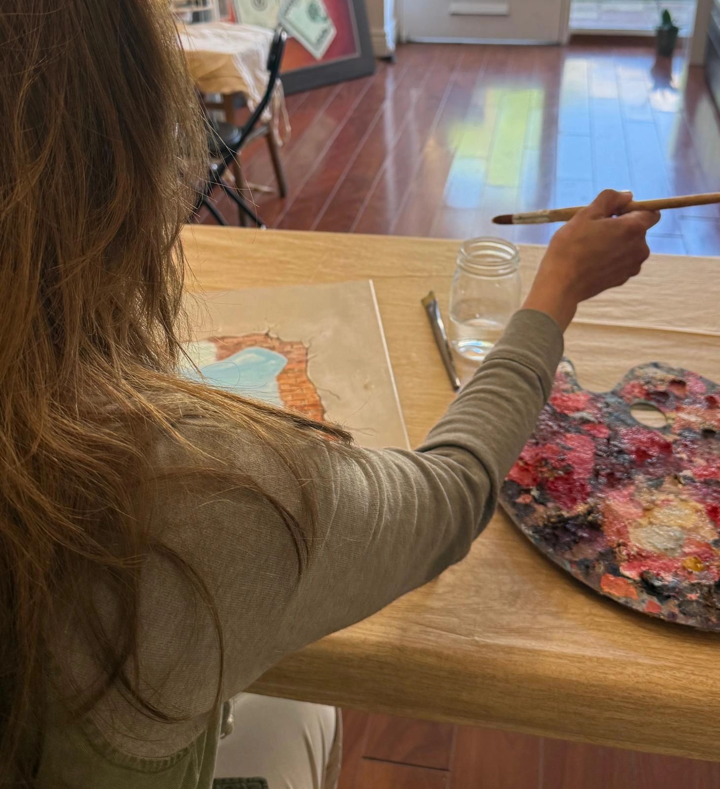 Person painting with a brush at a table with a colorful palette.