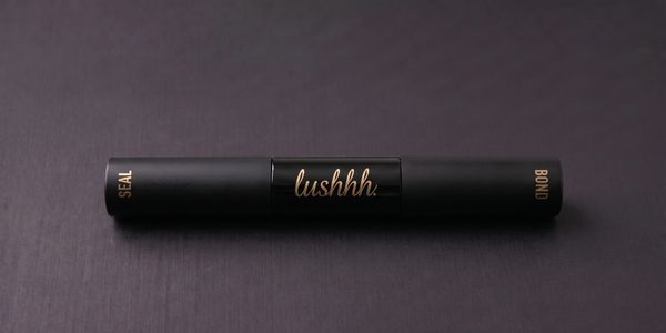 A sleek black pen with gold lettering reading 'lushhh' on a dark surface.