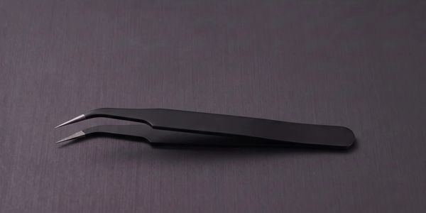 Black angled tweezers on a dark textured surface.