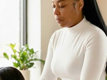Woman in white outfit giving a shoulder massage to another woman indoors.
