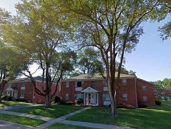 A residential brick apartment building surrounded by trees and lawns.