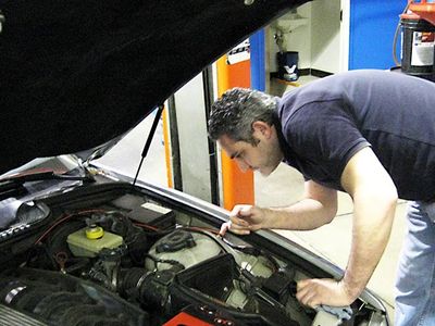Man inspecting car engine with diagnostic tool in a garage.