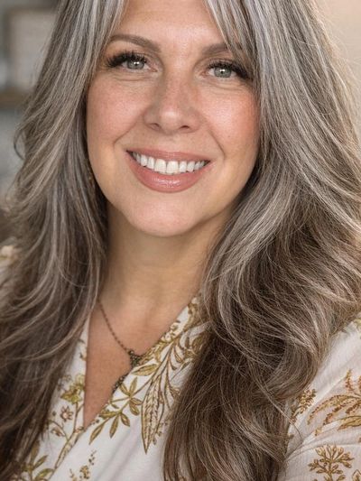 Smiling woman with long, wavy gray hair and a floral blouse.