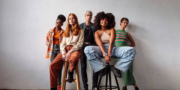 A diverse group of five young adults posing confidently against a plain wall.