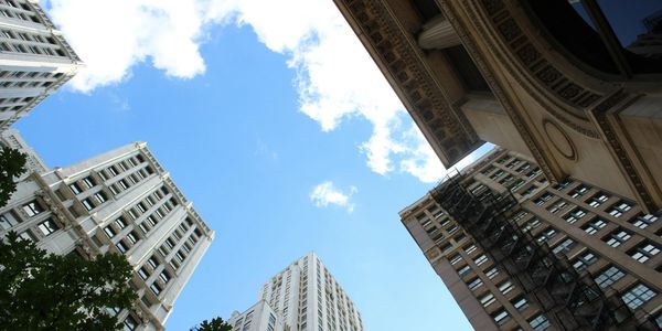 Upward view of skyscrapers against a bright blue sky with some clouds.