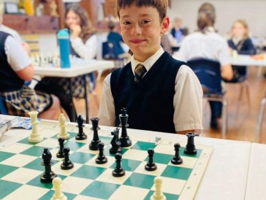 Young boy in school uniform playing chess in a classroom setting.