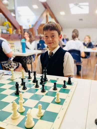 Young boy in school uniform playing chess in a classroom setting.