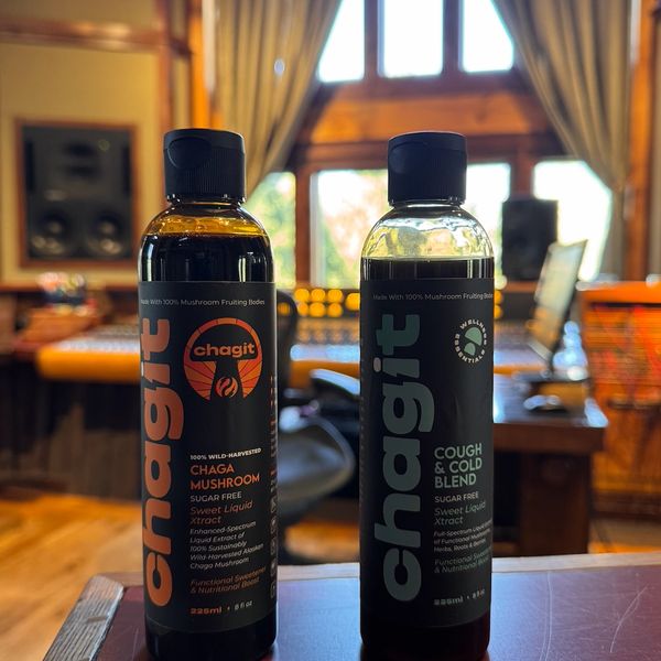 Two bottles of Chagit mushroom elixirs on a table in a cozy room.