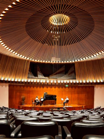Sala de conciertos con techo artístico y músicos en el escenario.