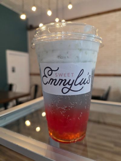Colorful layered drink in a Sweet Emmylu's cup on a reflective surface.