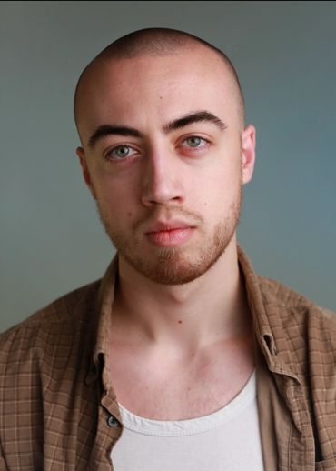 Portrait of a young man with a shaved head and green eyes.