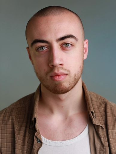 Close-up portrait of a young man with a shaved head and light beard.