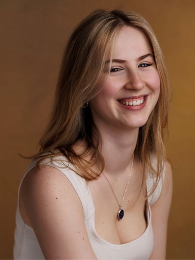 Young woman with blonde hair smiling warmly against a brown background.