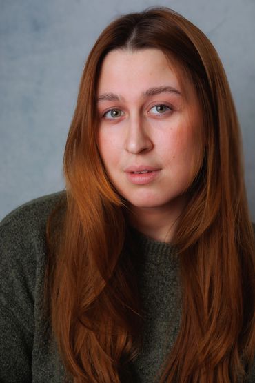 Portrait of a young woman with long red hair and a green sweater.