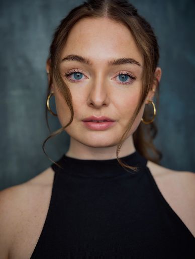 Close-up portrait of a woman with blue eyes and gold hoop earrings.