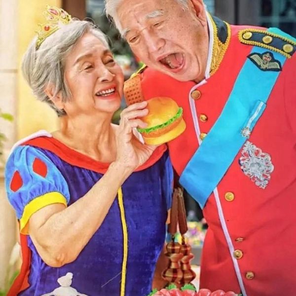 Elderly couple in royal costumes playfully sharing a burger.