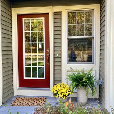 Cozy front porch with a red door, potted plants, and a welcome mat.