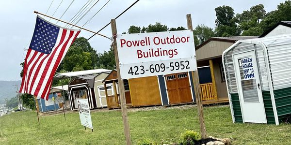 Display of outdoor buildings for sale with an American flag and signage.