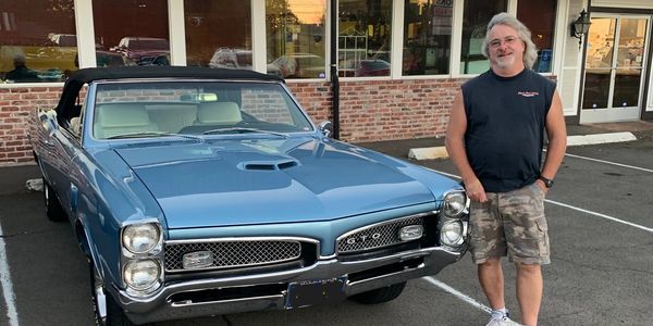 Man standing next to a blue vintage convertible car.