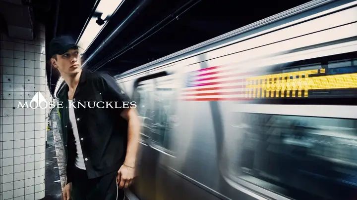 A man stands on a subway platform as a train zooms past.