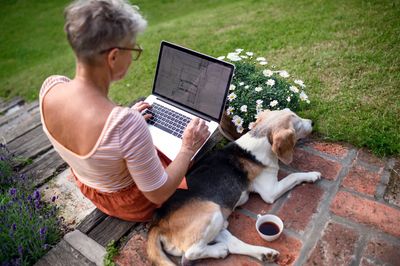 Woman using a laptop, with her dog at her side.