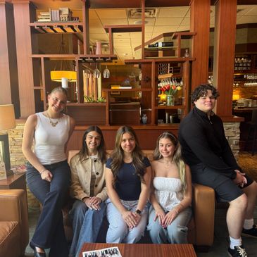 Five friends posing together in a cozy cafe with warm wooden decor.