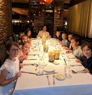 Group of children and an adult seated at a long dining table in a cozy restaurant.