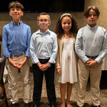 Four well-dressed children standing side by side indoors.