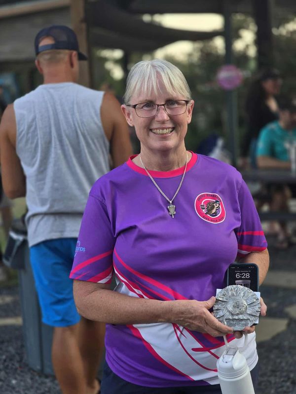 Smiling woman in a purple sports shirt holding a trophy outdoors.
