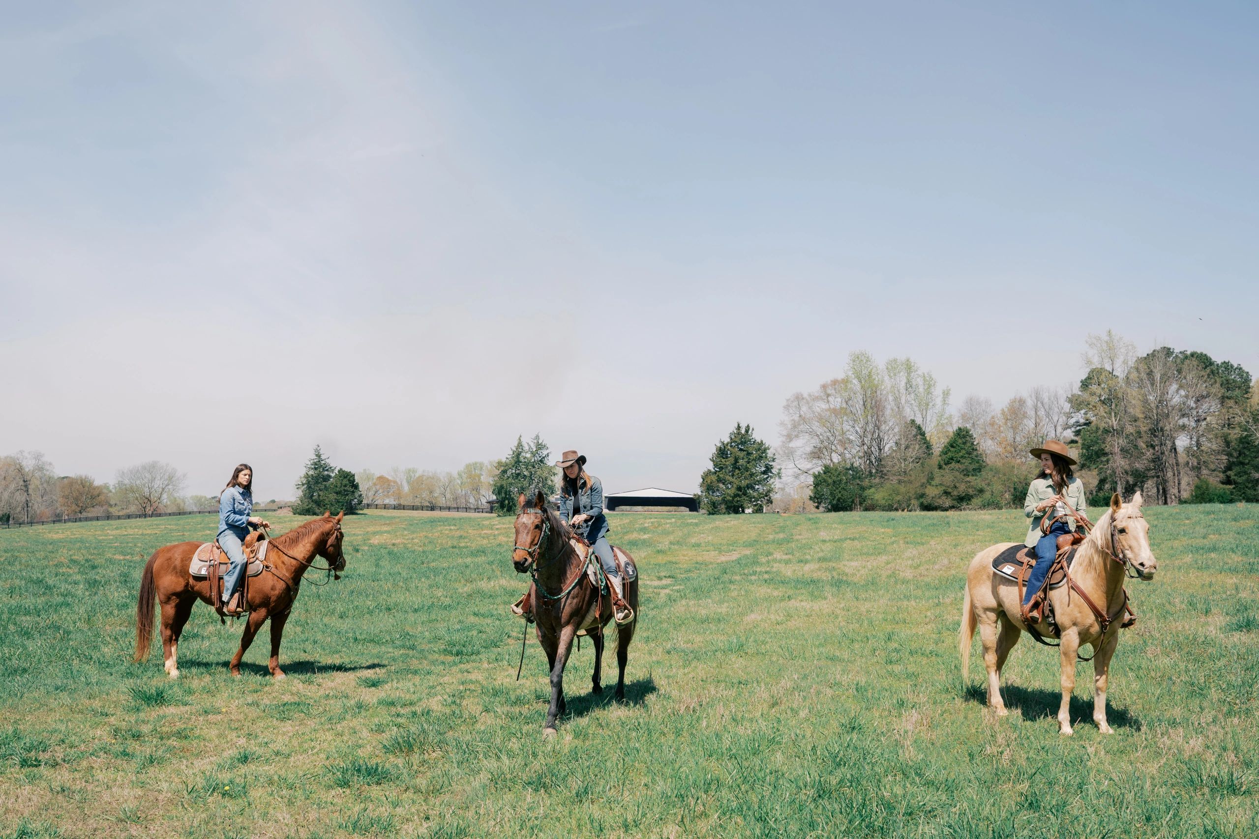 Three women on horseback in a grassy field under a clear sky.