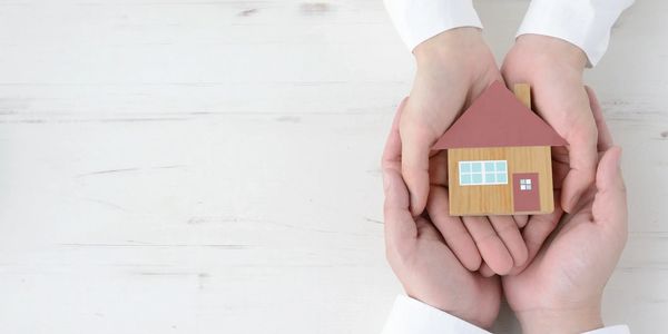Hands holding a small wooden house model symbolizing protection and care.