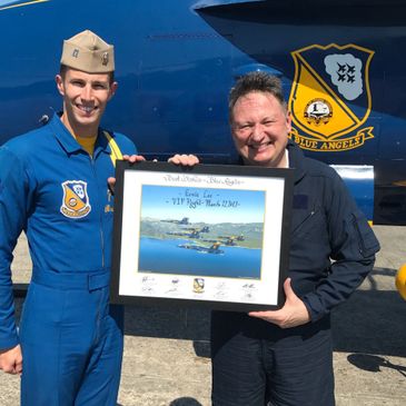 Two men in front of Blue Angels jet, holding framed photo.