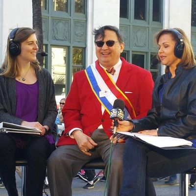 Three people engaged in an outdoor interview, one wearing a red jacket with a sash.