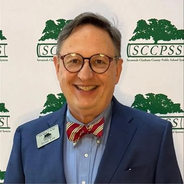 Man in suit with bow tie smiling in front of SCCPSS backdrop.