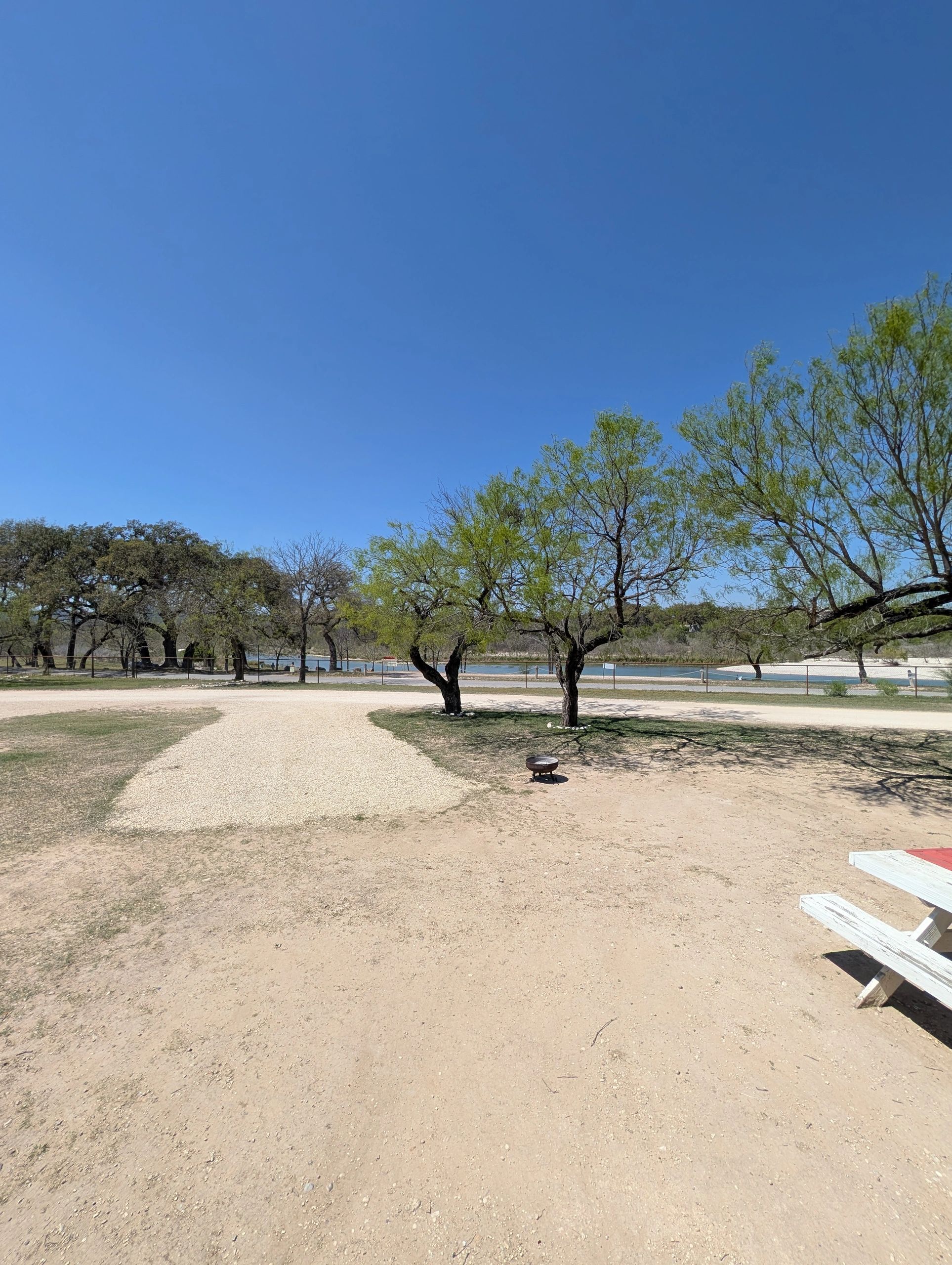 Clear blue sky over a park with dirt paths, trees, and a picnic table.