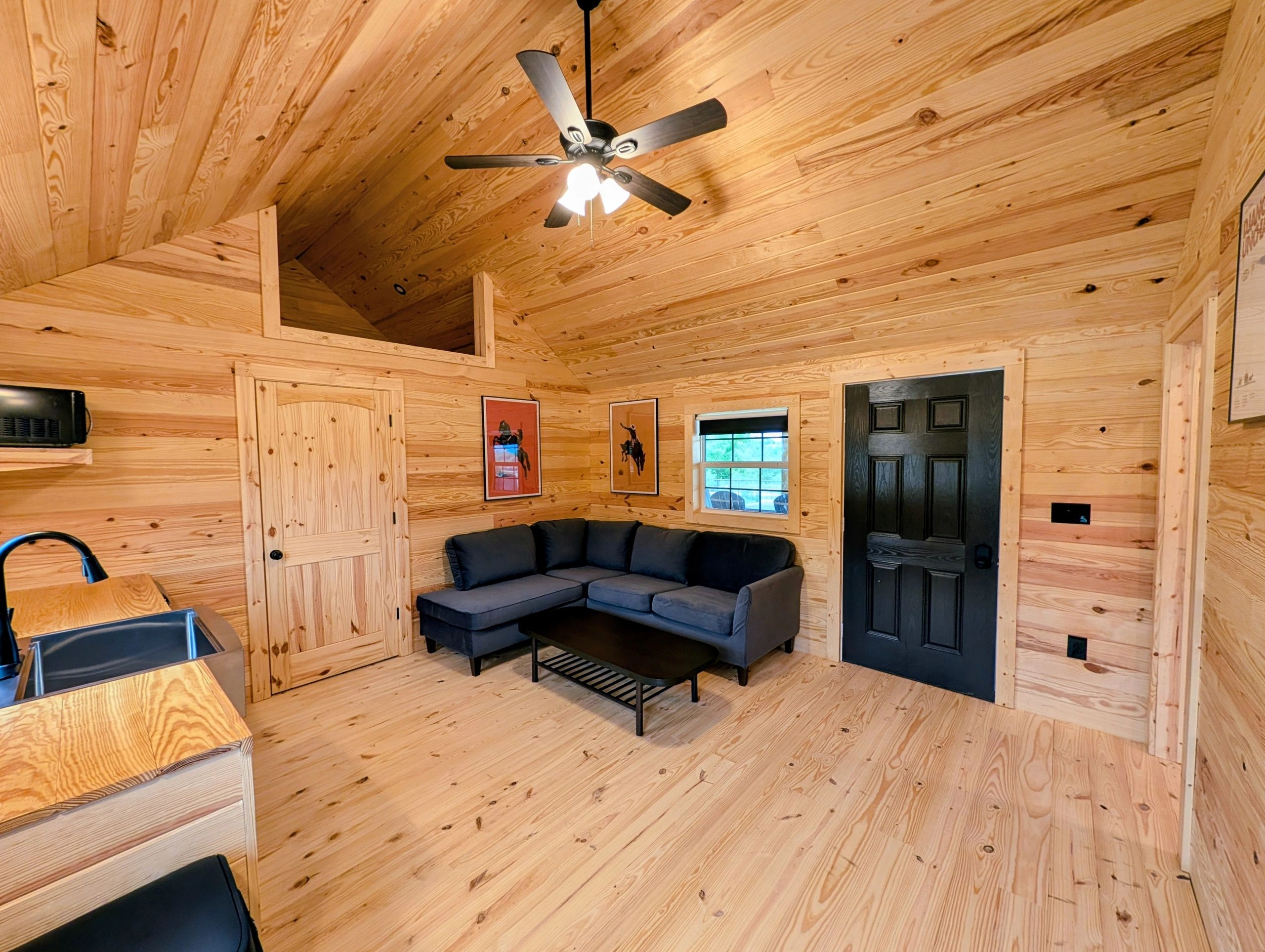 Cozy wooden cabin interior with a black couch and ceiling fan.