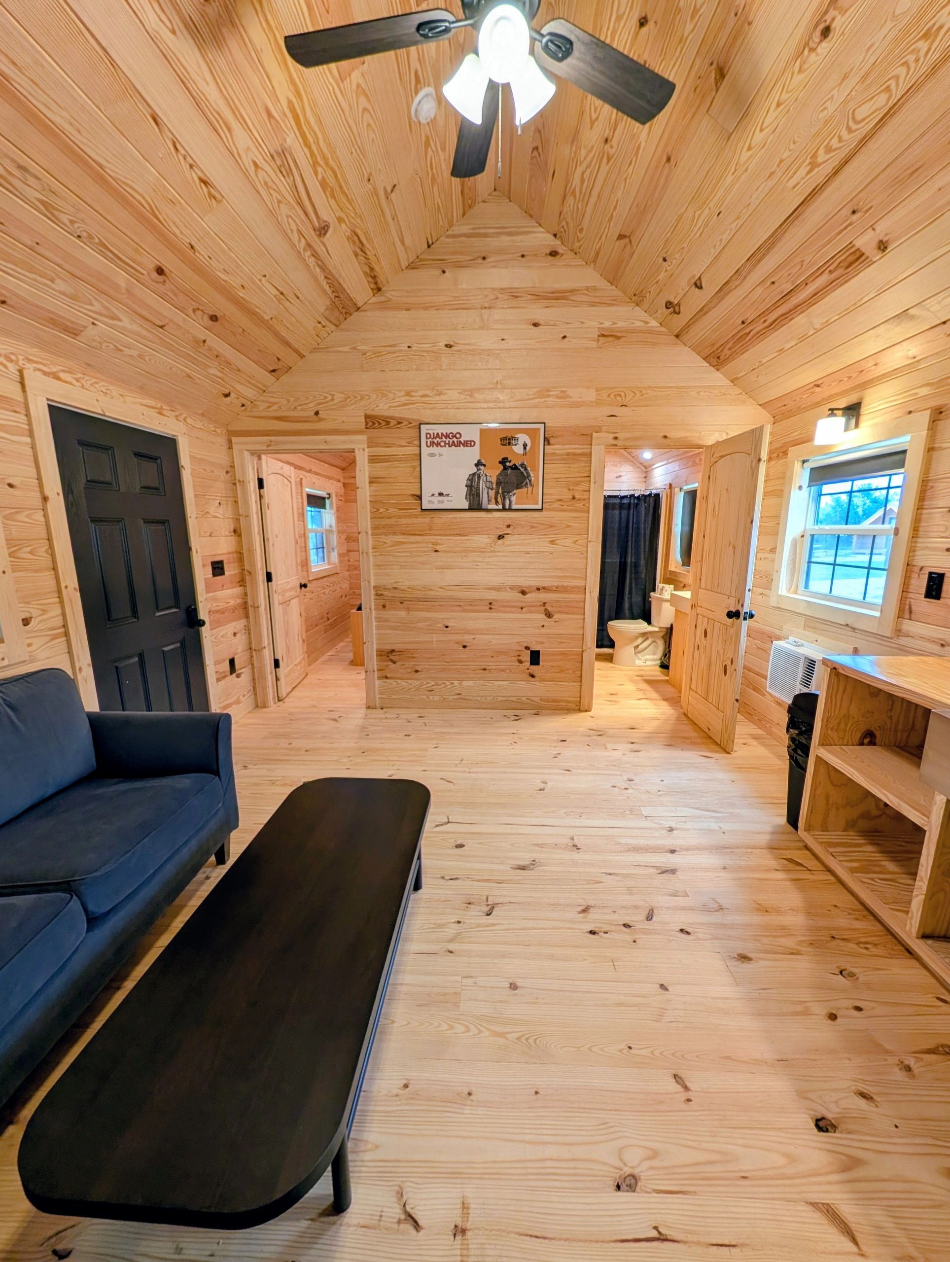 Cozy wooden cabin interior with black furniture and ceiling fan.