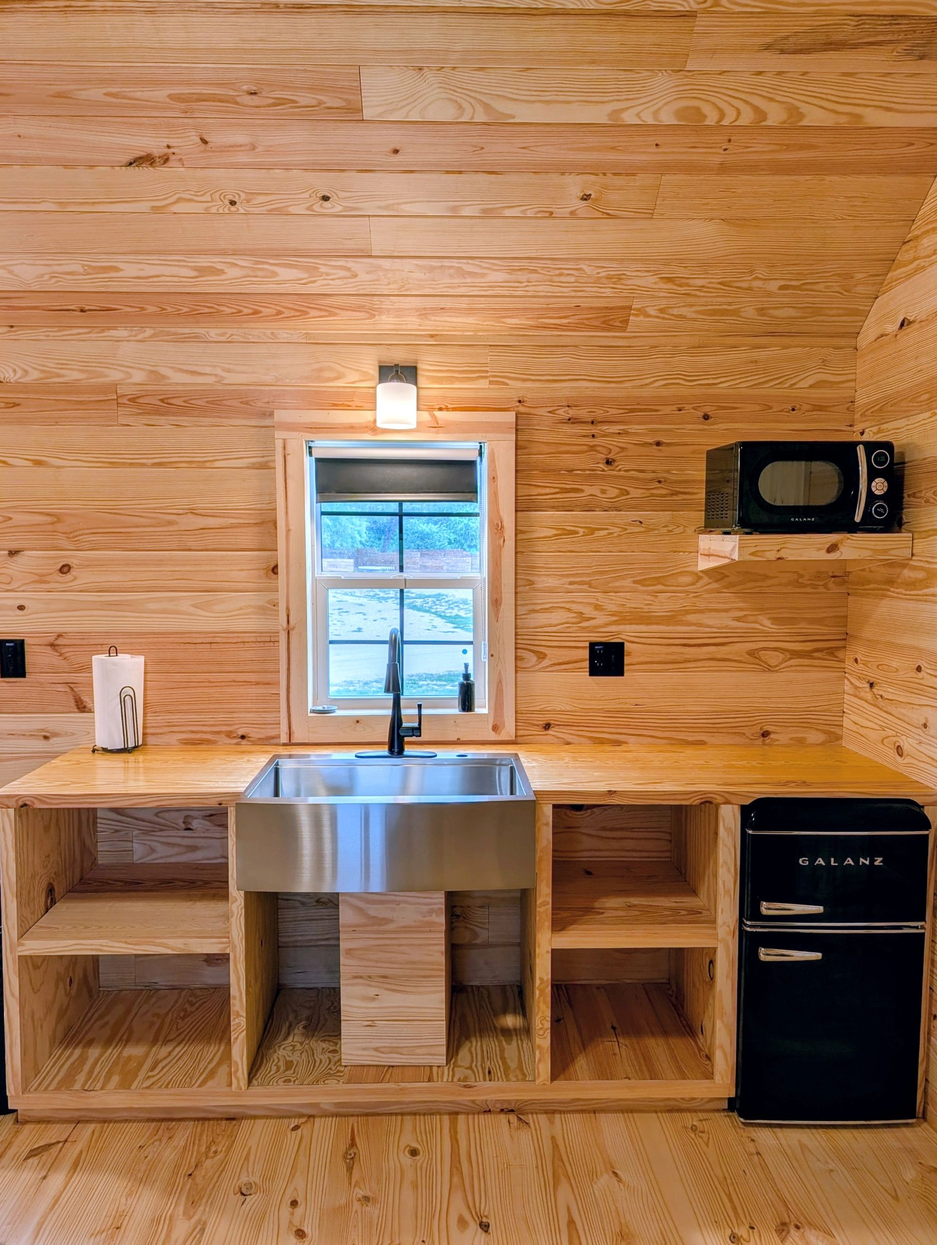 Rustic kitchen with wood walls, stainless steel sink, and black appliances.