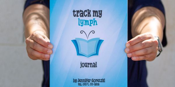 Woman smiling, holding a blue 'track my lymph journal' book.