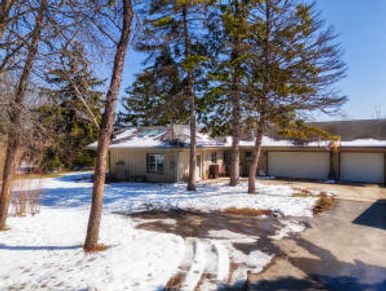 Snow-covered suburban house with tall trees on a clear winter day.
