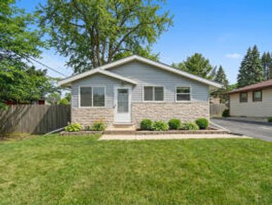 Small single-story house with a well-maintained lawn and clear blue sky.