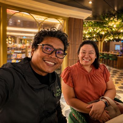 Two people smiling inside a warmly lit restaurant or cafe.