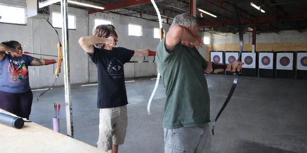 Three people practicing archery indoors aiming at targets.