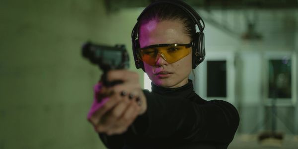Woman aiming a handgun while wearing protective glasses and earmuffs.