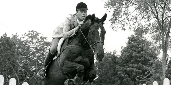 A rider in classic attire jumps a horse over an obstacle outdoors.