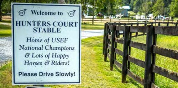 Sign welcoming visitors to Hunters Court Stable with a message about happy horses and riders.